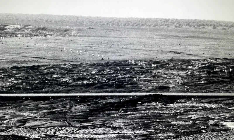 Archival photo of a line of people hiking across a volcanic crater.